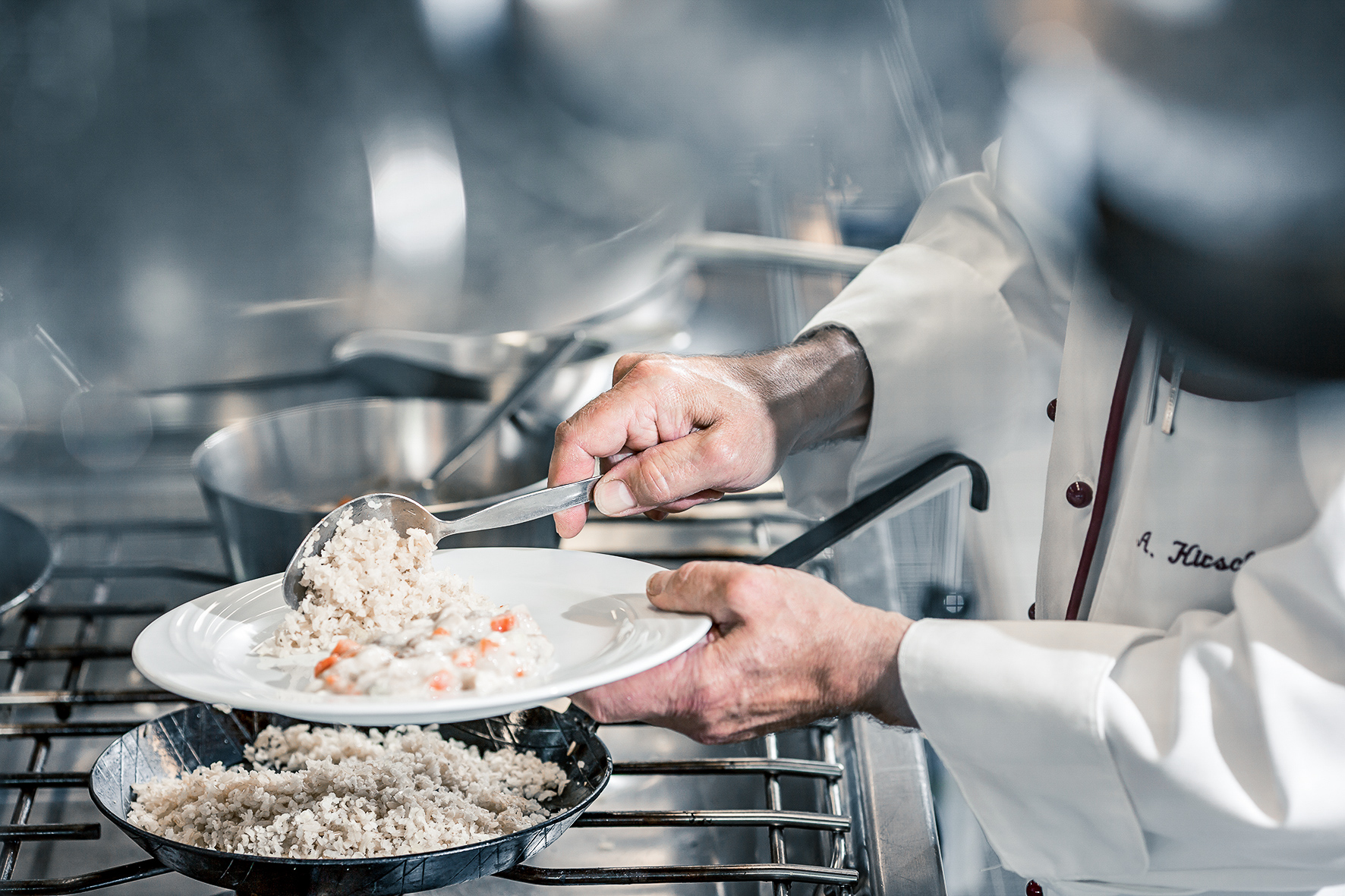 Koch schöpft Essen aus der Pfanne in einen Teller